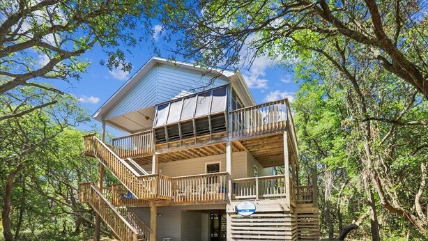 Une cabane à deux étages avec un balcon, entourée d’arbres.