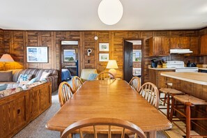 Ein gemütliches Wohnzimmer mit einem Holzespeisebereich, Stühlen, einer Couch und einer Küchenzeile mit Holdekor und Geräten.