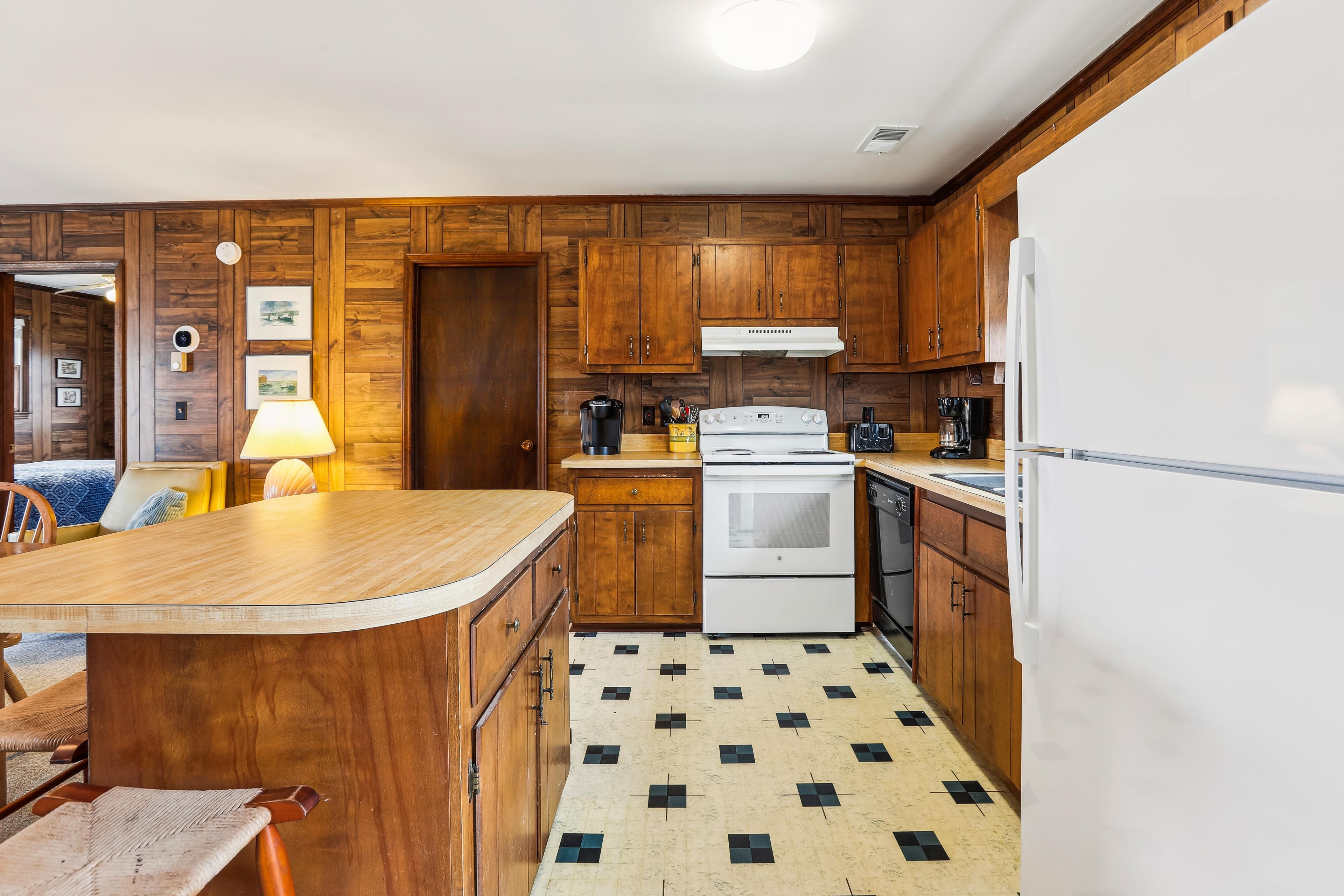 A compact kitchen with wooden cabinets, a central island, a built-in oven, and a refrigerator.