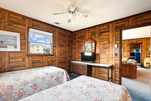 Ein Zimmer mit Holzwandverkleidung, zwei Betten mit blumigem Bettzeug, einem Schreibtisch mit Fernseher und einem Fenster mit Blick auf Gebäude.