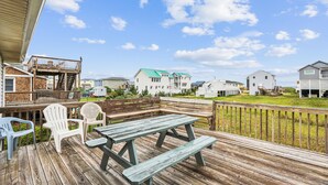 A wooden deck with picnic tables and chairs, overlooking a coastal residential area with houses and a clear sky. - Herons Return -- Flexible Arrival and Stay Dates Year Round (Kitty Hawk)