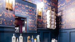 Un baño con pared azul, un lavamanos blanco, un inodoro y una repisa con toallas y artículos de aseo.
