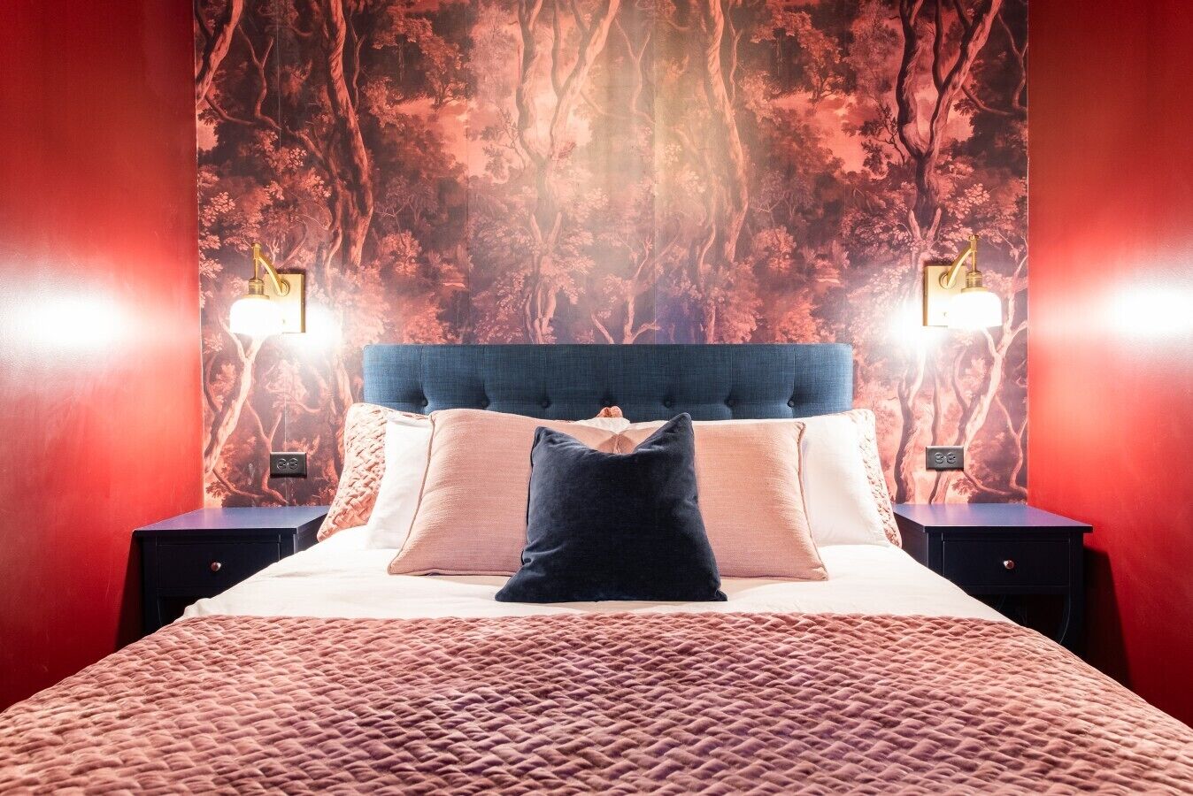 Un dormitorio con una cama grande, dos mesitas de noche y una pared decorada con un diseño de árboles.