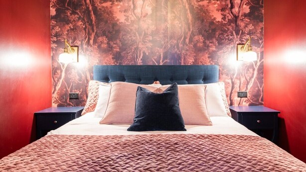 Un dormitorio con una cama grande, dos mesitas de noche y una pared decorada con un diseño de árboles.