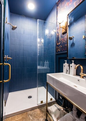 Un baño con cabina de ducha de vidrio, un lavabo blanco con detalles dorados y un espejo con estampado de mariposa.