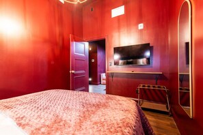 Ett hotellrum med en stor säng, en tv som är monterad på väggen och en dörr som leder till ett annat rum.