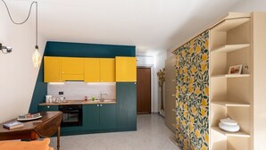 Een compacte keuken met turquoise en gele kastjes, een witte spatwand en een houten eettafel met een boek erop.