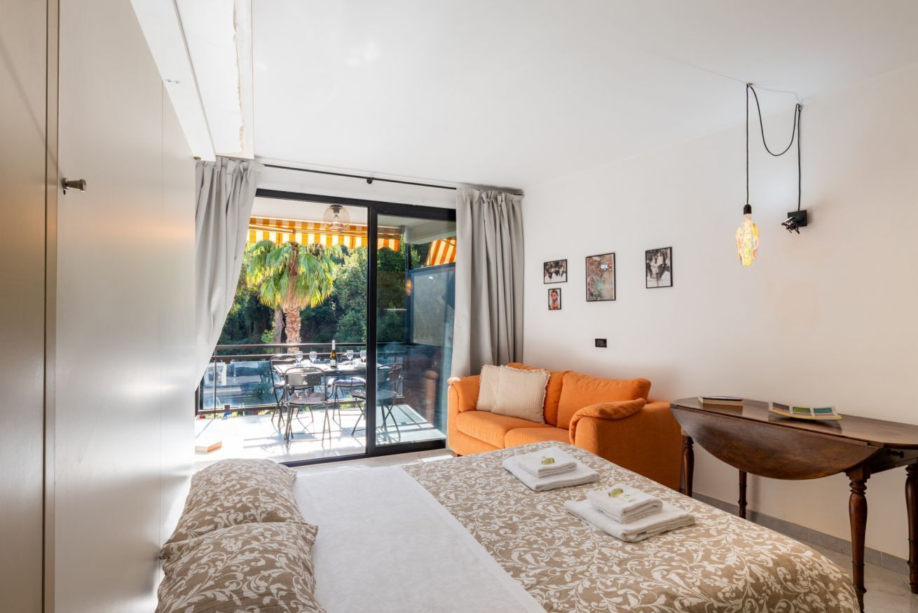 Une chambre d’hôtel moderne avec un grand lit, un canapé orange, une petite table et un balcon donnant sur un paysage verdoyant.