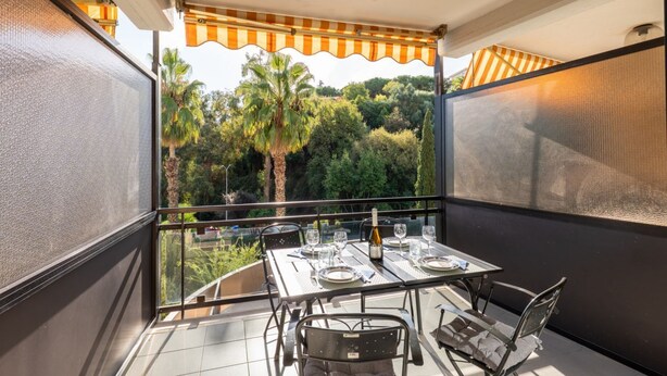 Een balkon met een tafel gedekt voor twee personen, een fles wijn en uitzicht op groen.