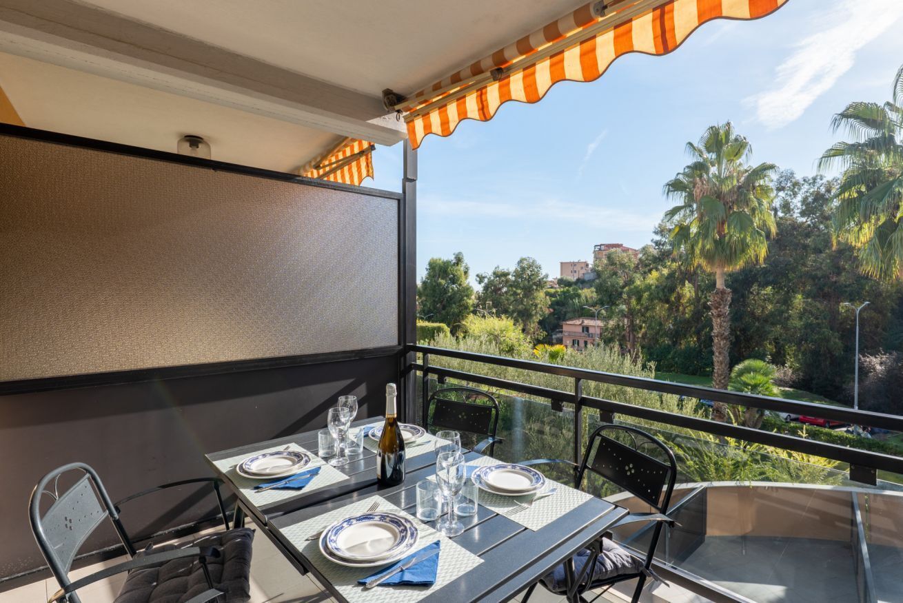 Un balcon avec une table dressée pour deux personnes, une bouteille de vin et une vue sur les palmiers et les bâtiments.