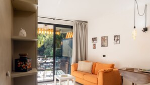 Een moderne woonkamer met een bank, een klein tafeltje en uitzicht door een glazen deur op een buitengebied.