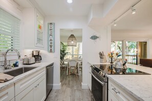 A modern kitchen with white cabinetry, a built-in oven, and a dining area with wicker chairs. - Bike to the Beach! Serene 1BR Sea Pines Condo / Pet Friendly! (Hilton Head Island)