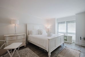 A bedroom with a bed, bedside tables, a chair, and a window with blinds. - Bike to the Beach! Serene 1BR Sea Pines Condo / Pet Friendly! (Hilton Head Island)