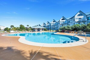 A hotel with a large swimming pool, multiple balconies, and a well-maintained lawn area. - Gulf Front | Community Pools | Beach Boardwalk (Gulf Shores)