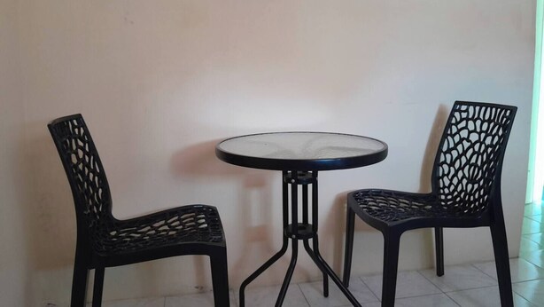 Uma pequena mesa redonda com estrutura de metal preta e duas cadeiras pretas com desenhos recortados detalhados.