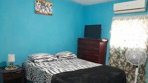 Quarto com cama, penteadeira, mesa de cabeceira, ar condicionado e ventoinha.