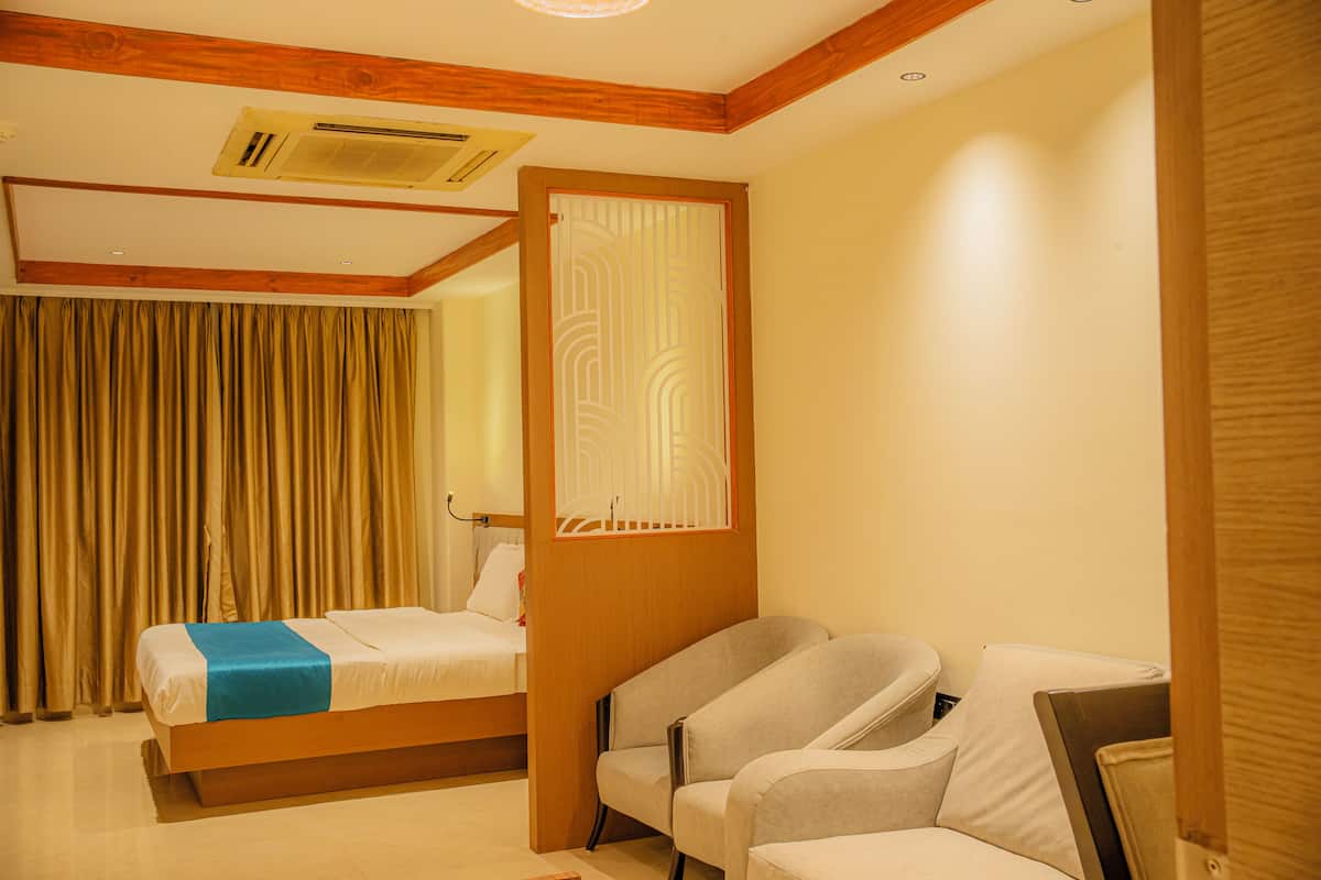 A hotel room with a bed, a desk, two chairs, a wooden headboard, and a window with curtains.