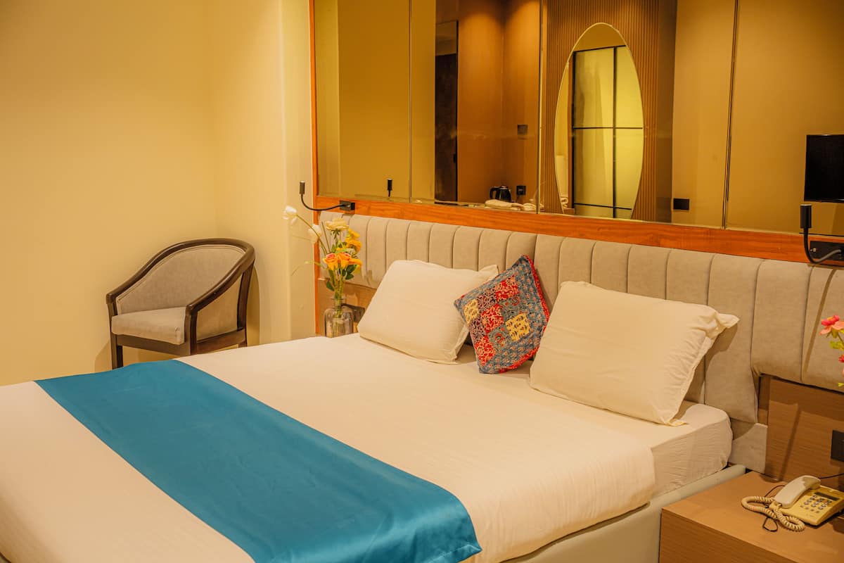 A hotel room with a bed, a chair, a bedside table with a phone, and a mirror above the bed.
