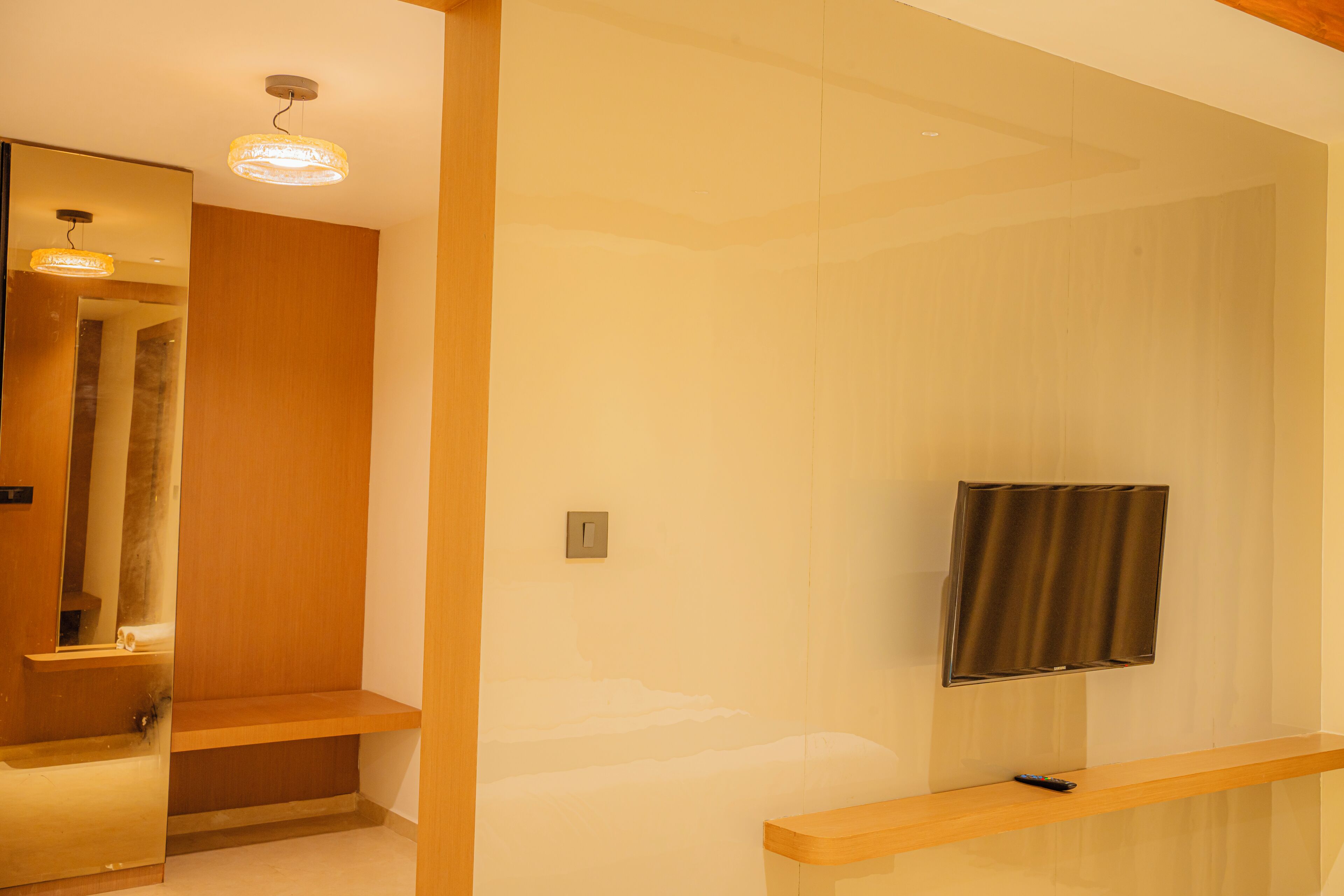 Un baño moderno con tocador de madera, espejo, televisor montado en la pared y lámpara en el techo.