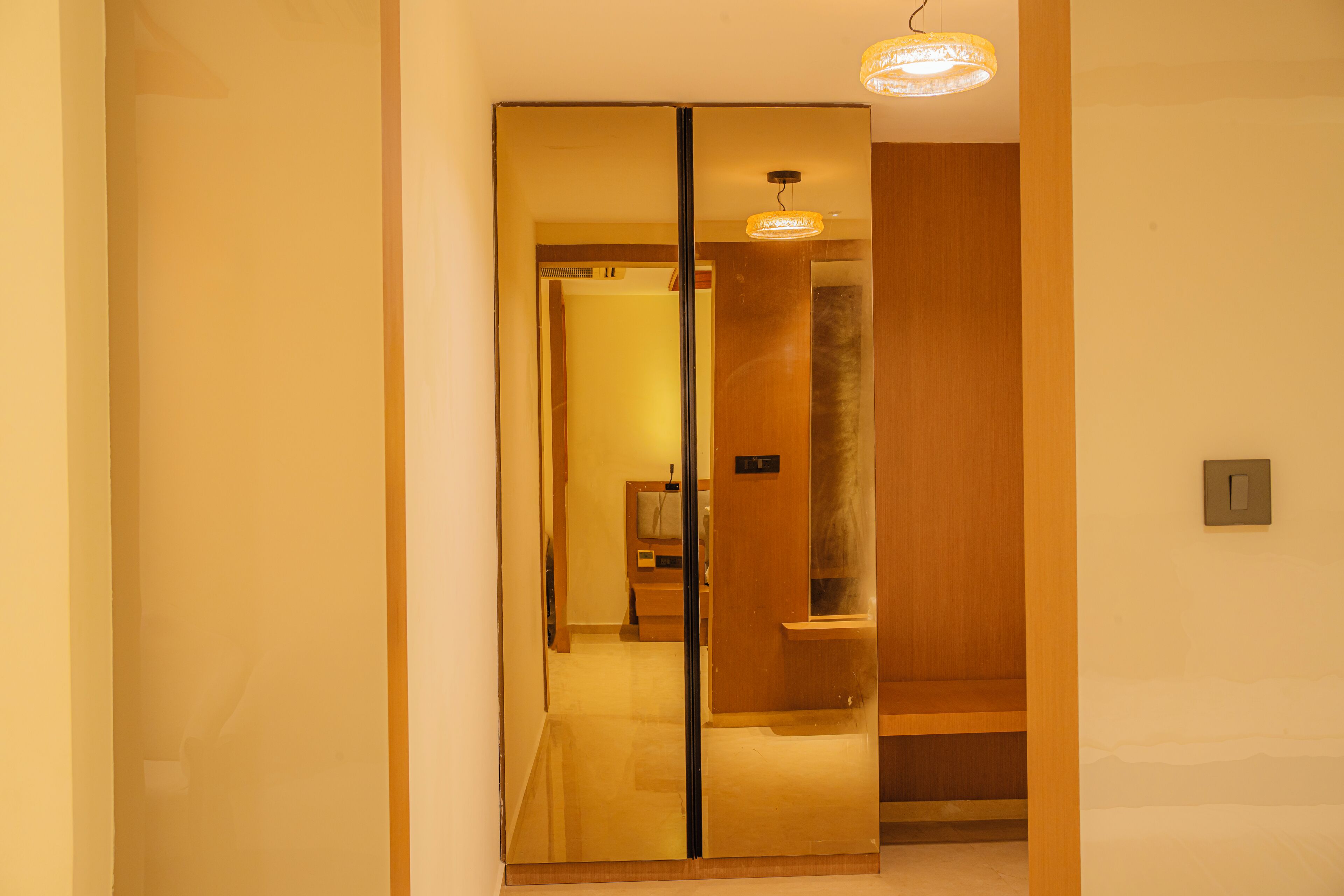 A hallway with a mirrored wall, a wooden door, and a ceiling light fixture.