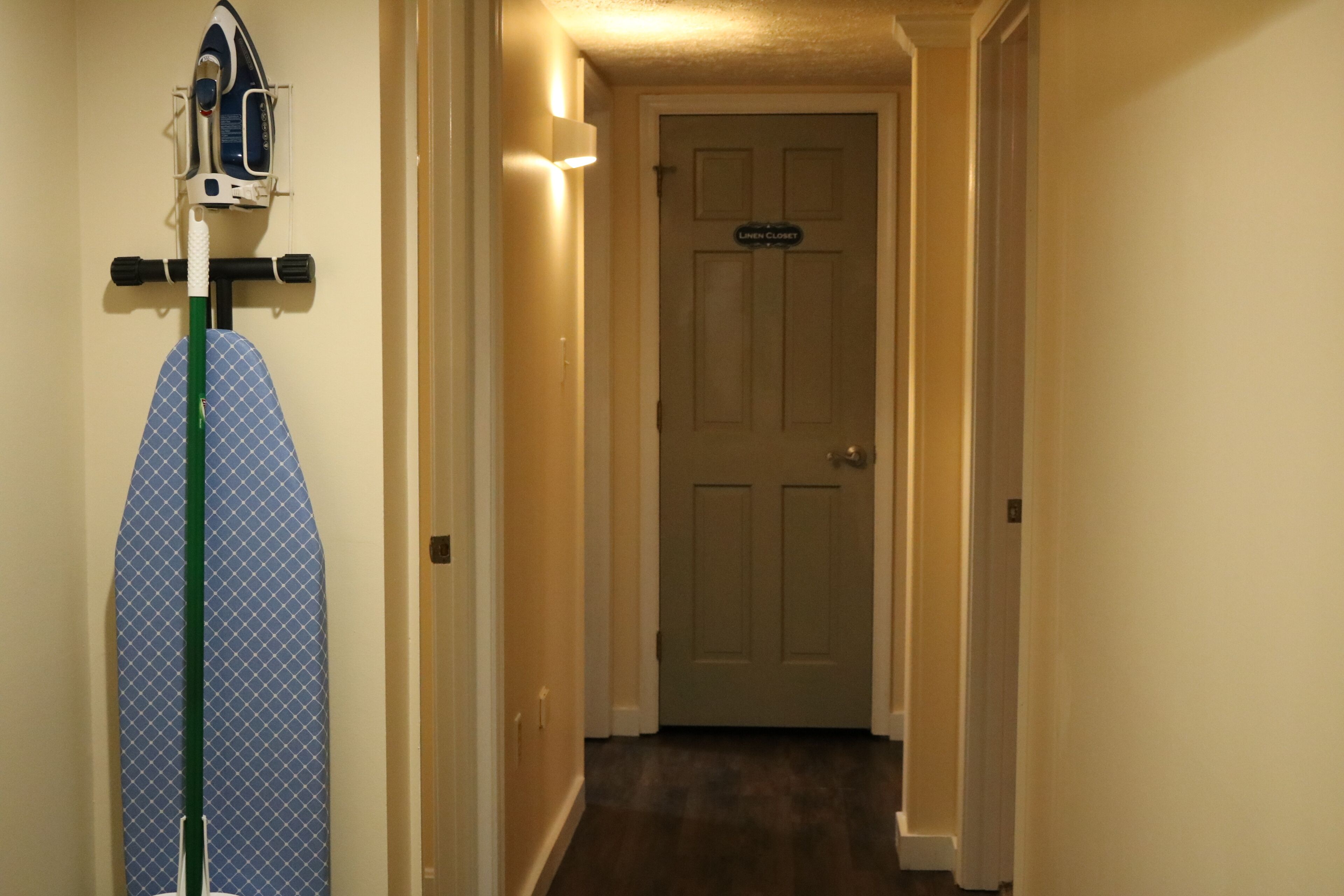 Un couloir avec une porte sur laquelle est inscrit « garde-linge » et une planche à repasser avec un fer à repasser et le plateau.
