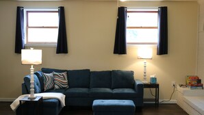 A living room with a dark blue sofa, a matching ottoman, two lamps, and a window with curtains. - Smallwood St Park,Washington DC and Indian Head (Marbury)