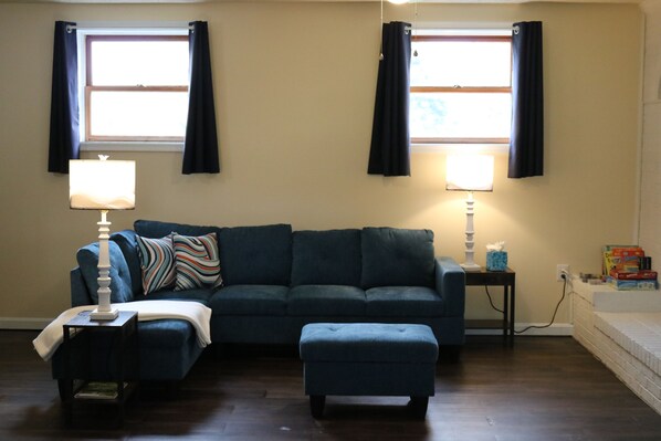 A living room with a dark blue sofa, a matching ottoman, two lamps, and a window with curtains. - Smallwood St Park,Washington DC and Indian Head (Marbury)