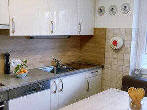 Eine Küche mit weißen Schränken, einer Edelstahlspüle, einer Holzarbeitsplatte und einer Wanduhr.