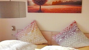 Quarto com cama, travesseiros, uma luminária na parede e um quadro de uma árvore.