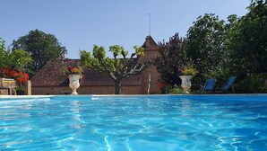 A clear swimming pool with a tiled deck, surrounded by trees and a building with a tiled roof. - Exceptional gîte in the heart of a 12-hectare natural estate (Le Buisson-de-Cadouin)