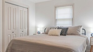 A bedroom with a bed, bedside tables, a ceiling fan, a window with blinds, and a door.