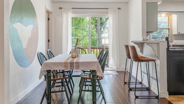 A dining area with a table set for six, a kitchen area with a refrigerator, and a view of greenery outside.