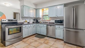 A kitchen with light blue cabinets, stainless steel appliances, and a tiled floor.