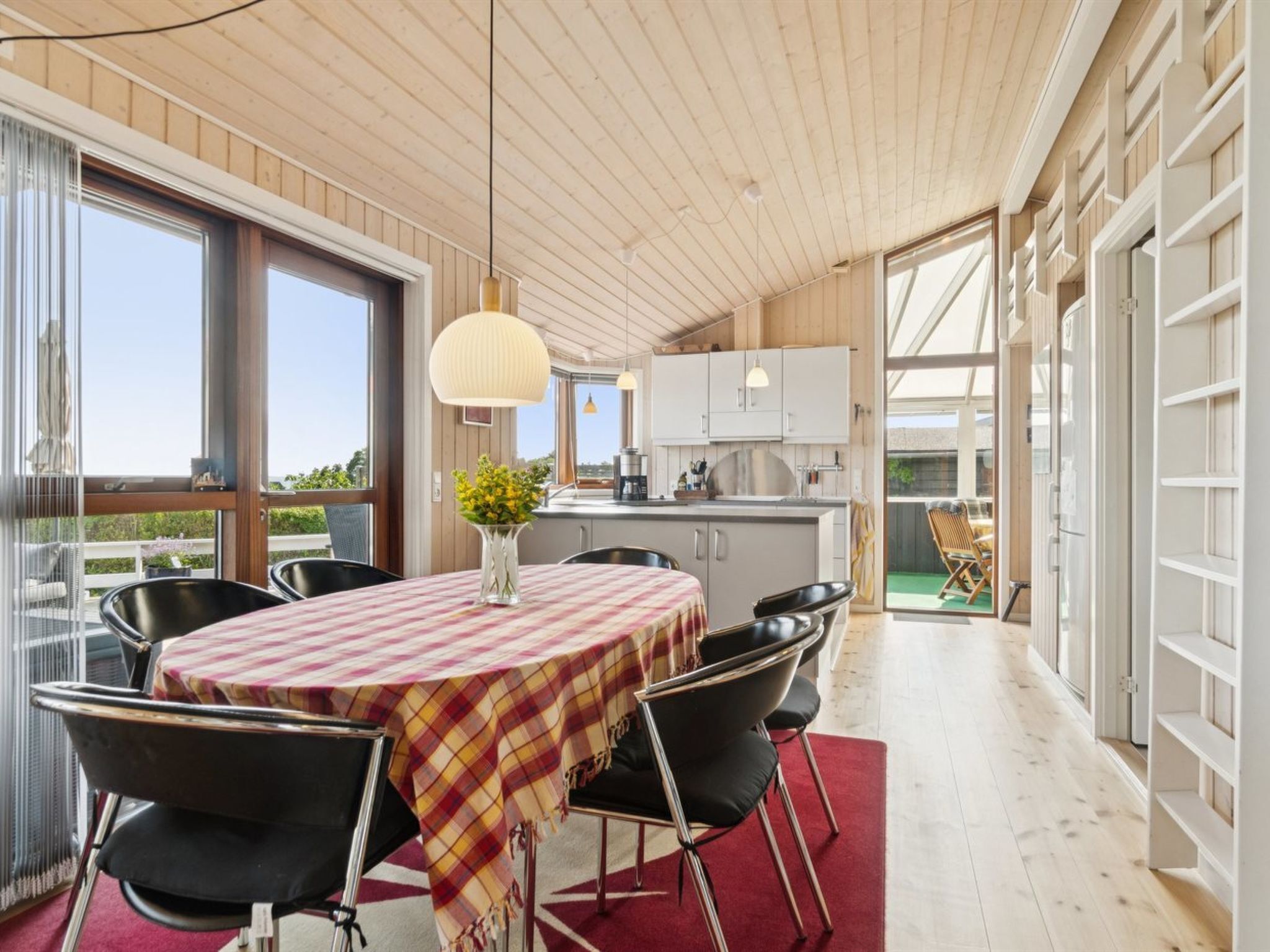 A modern kitchen with white cabinets, a central island, and a dining area with a red and yellow checkered tablecloth.