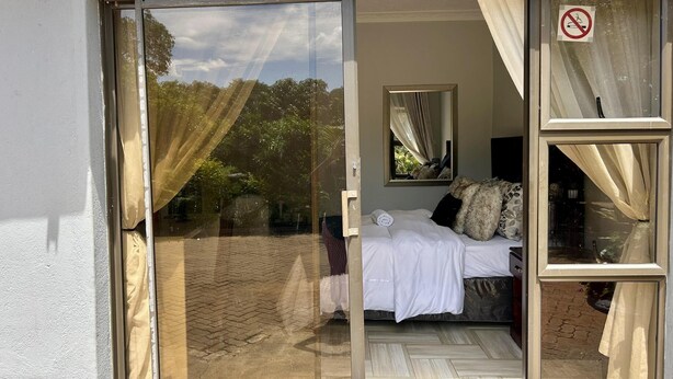 A room with a bed, a window with curtains, a mirror, and a door.