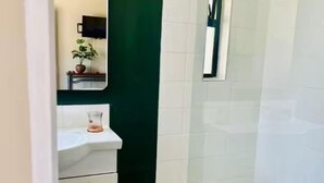 Ein modernes Badezimmer mit einem weißen Waschbecken, einem Spiegel, einer grünen Akzentwand und einer Duschkabine aus Glas.