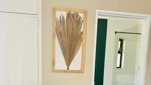 Ein grauer Stoffclubstuhl mit Holzgestell, ein gerahmtes Kunstwerk an der Wand und ein durchgehender Durchblick in ein Badezimmer.
