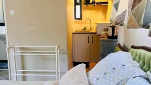 Ein kleines Schlafzimmer mit Bett, einer kompakten Küchenzeile und einem Badezimmer.