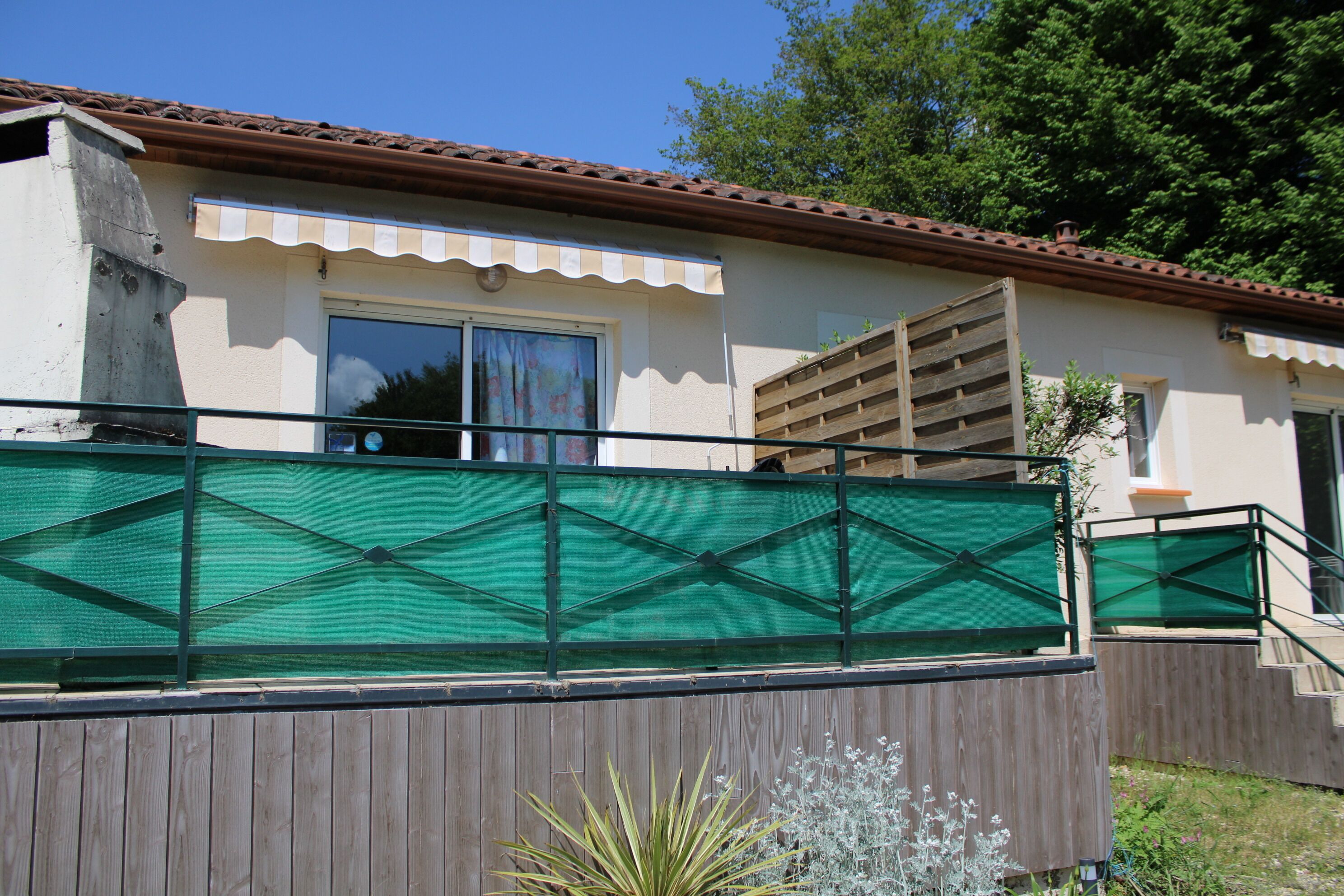 Un bâtiment avec un toit recouvert de tuiles, une clôture en bois et un écran de protection en treillis vert.