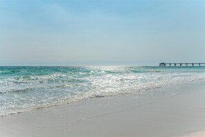 Ein Strand mit Wellen, einem Steg und blauem Himmel.