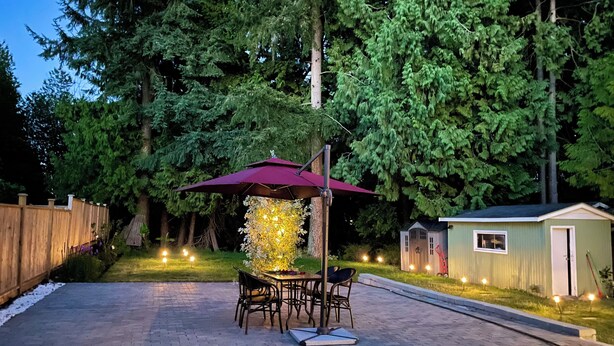 An outdoor patio with a table and chairs under a canopy, surrounded by trees and a small shed. - Metrotown sweet home 3-bedroom house in Burnaby perfect for your getaway (Burnaby)
