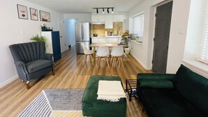 A compact living space with a kitchenette, a dining area, and a seating area with a green sofa and a dark armchair. - Metrotown sweet home 3-bedroom house in Burnaby perfect for your getaway (Burnaby)
