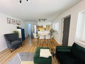 A compact living space with a kitchenette, a dining area, and a seating area with a green sofa and a dark armchair. - Metrotown sweet home 3-bedroom house in Burnaby perfect for your getaway (Burnaby)