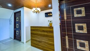 A reception area with a wooden reception desk, a dark wooden door with decorative panels, a chandelier, and a small potted plant. - Mangalam Retreat (Dhari)