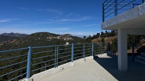 A concrete platform with a blue railing overlooking a mountainous landscape. - Mangalam Retreat (Dhari)