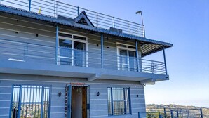 A two-story building with a balcony, a tiled entrance area, and a view of the landscape. - Mangalam Retreat (Dhari)
