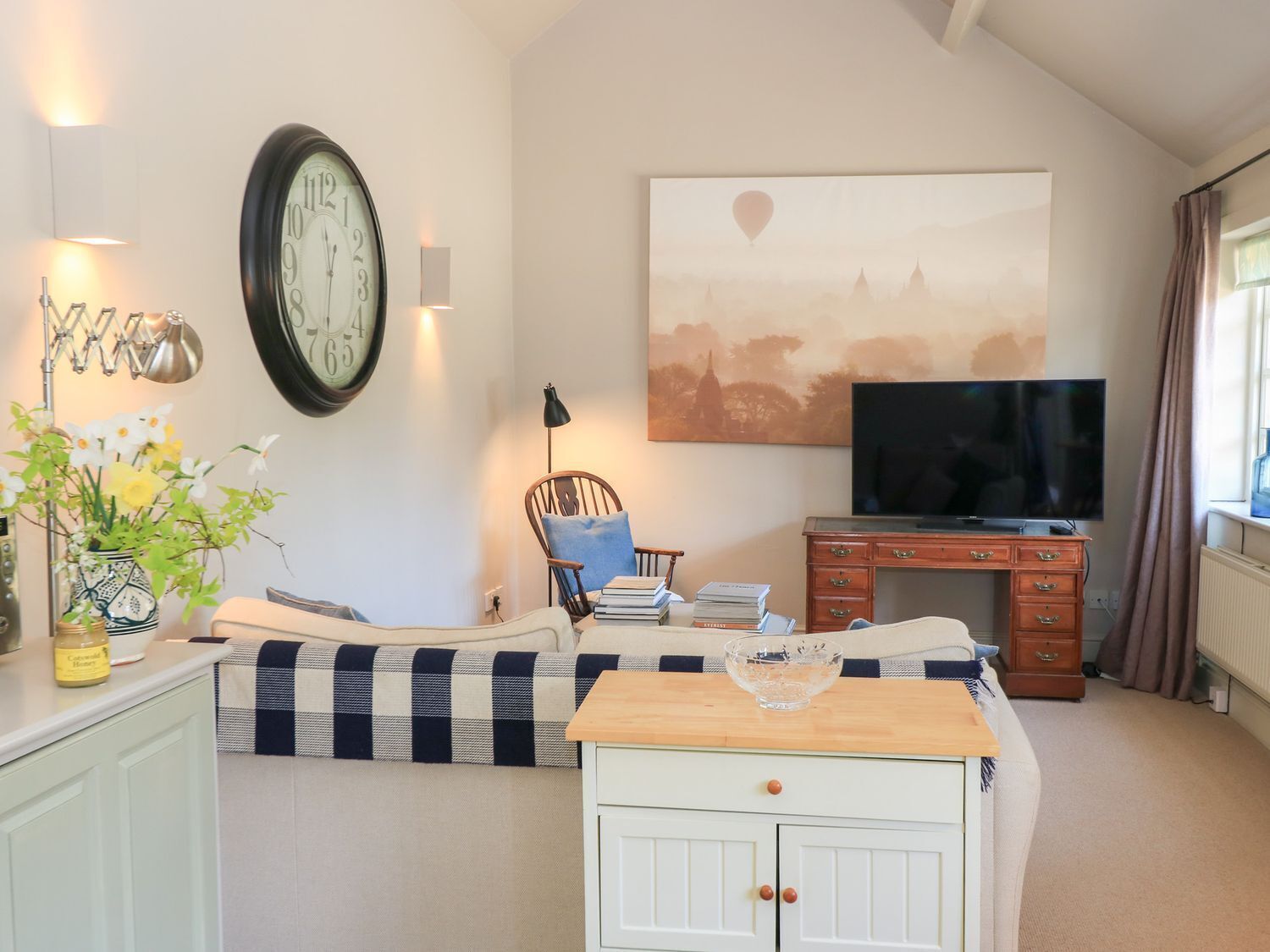 A cozy living room with a large clock, a television, and a painting of a hot air balloon.