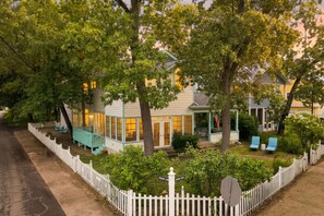 A two-story house with a porch, a small garden, and a white picket fence. - Juniper Presents: Sanctuary w/ Golf Cart, Resort Pools, Sandy Beach, Pickleball (Michigan City)