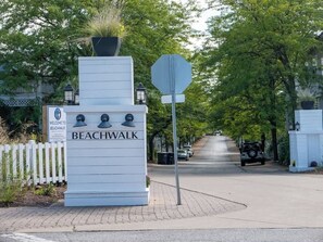 A sign for Beachwalk with a white background and black lettering, a stop sign, and a street lined with trees and parked cars. - Golf Cart, Resort Pools, Sandy Beach, Pickleball (Michigan City)