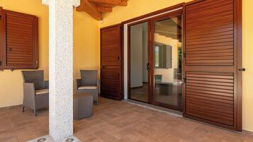 A covered patio area with two wicker chairs, a stone pillar, and a sliding glass door.